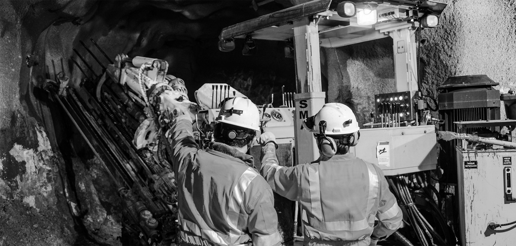 Two underground mine workers standing next to mine machinery